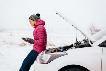 Man sitting on hood of broken down car in the cold